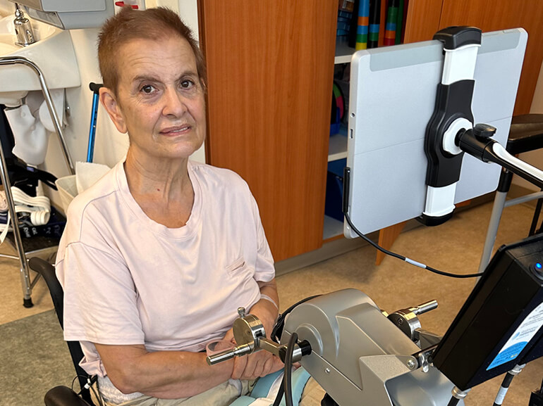 Ana Gomez Garcia smiles while sitting in front of a piece of rehabilitation equipment. 