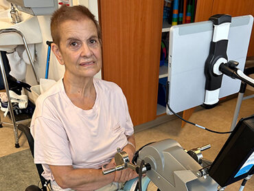 Ana Gomez Garcia smiles while sitting in front of a piece of rehabilitation equipment. 