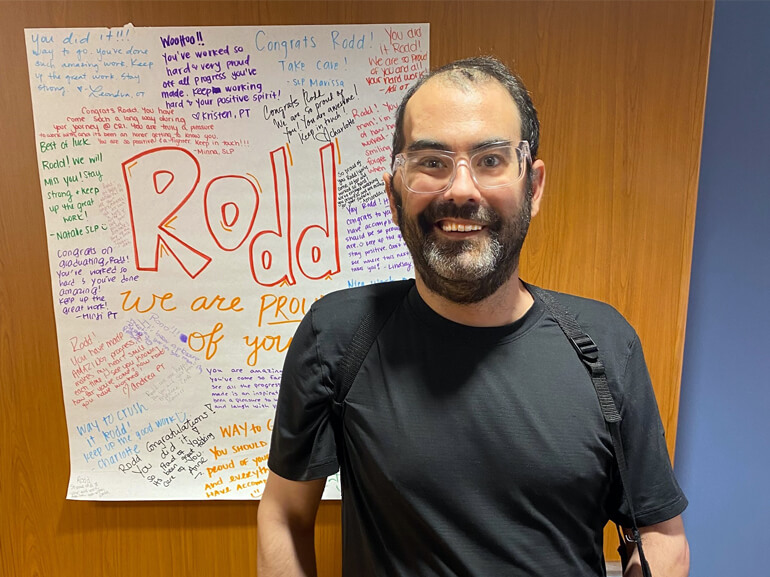 Rodd Zinberg stands smiling in front of a personalized poster with motivational messages.