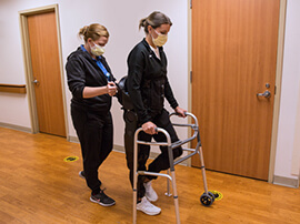 Therapist helps young female learning to use a walker