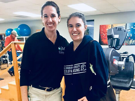 Helen in a black sweatshirt, smiling and standing with female physical therapist in therapy gym