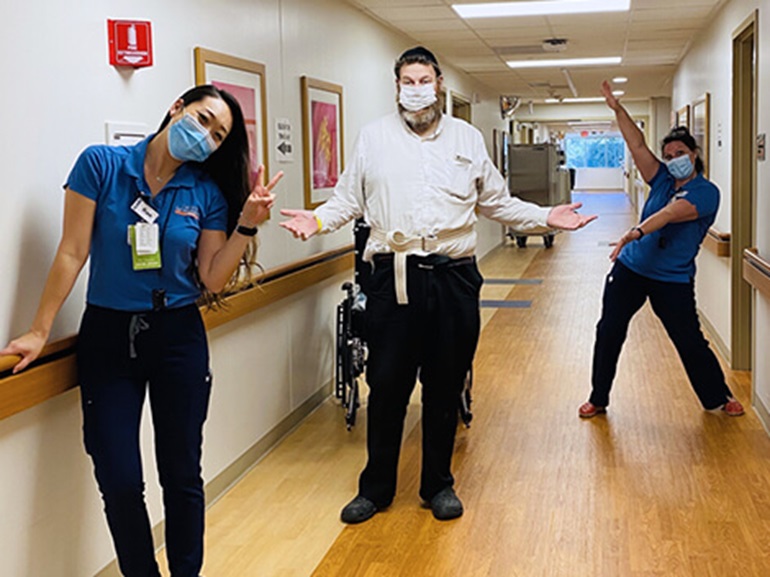 Alan in street clothes standing in hospital hallway with two female physical therapists