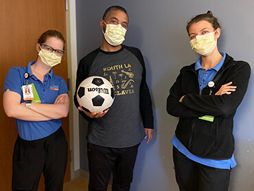 Rodney in street clothes holding a soccer ball and standing between two female nurses