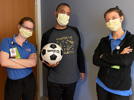 Rodney in street clothes holding a soccer ball and standing between two female nurses