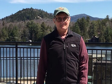 Bob wearing ball cap and standing in front of a lake on a sunny day